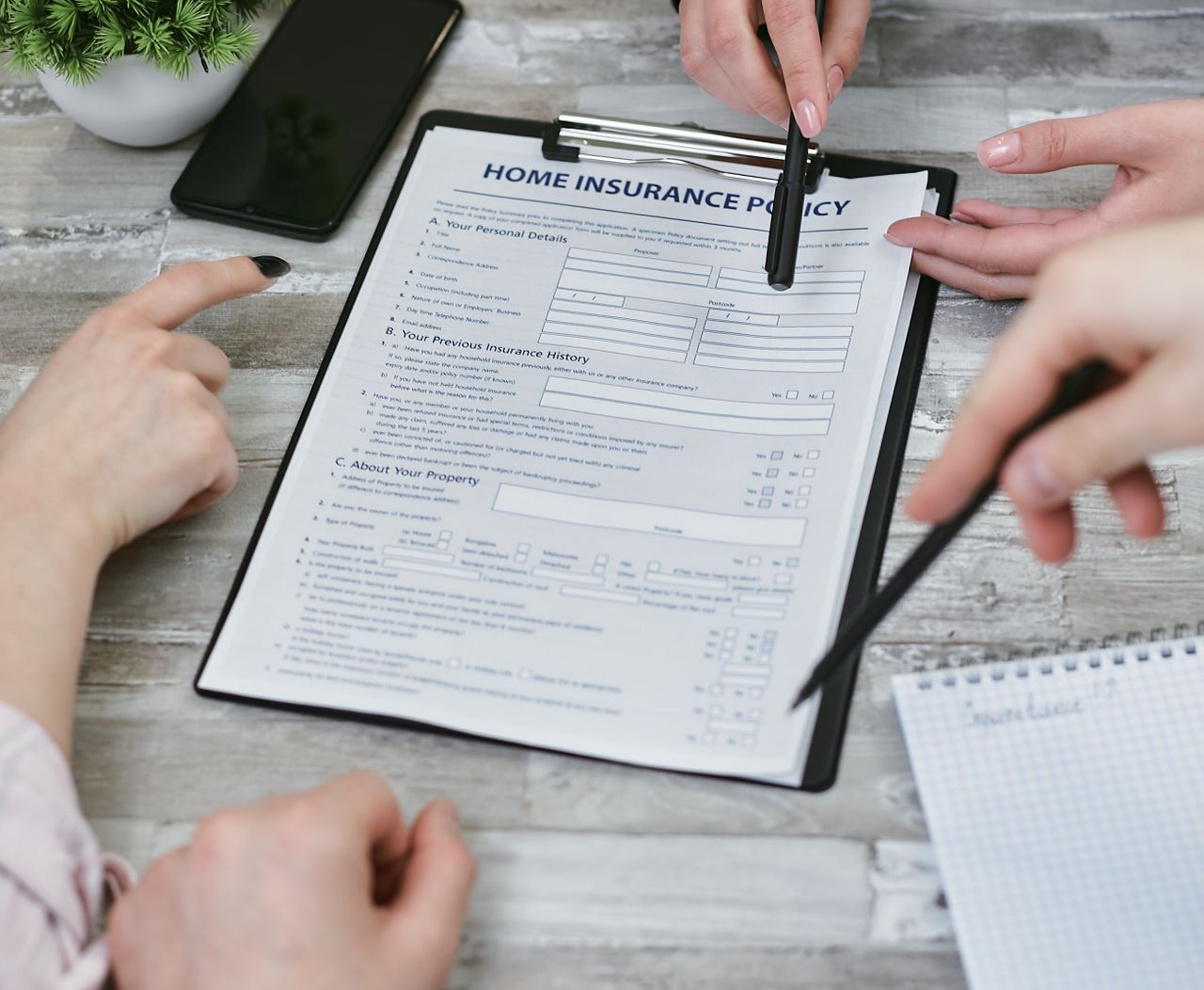 services-03 Three individuals collaborating on a home insurance policy document. Elements include a clipboard, notes, and pointing hands.